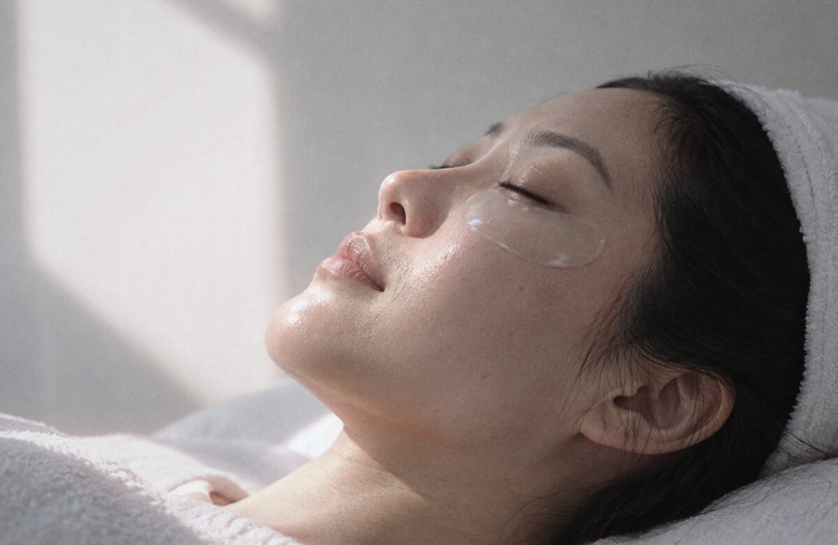 Woman lying on a facial bed with her eyes closed and a clear hydrogel patch under her eye