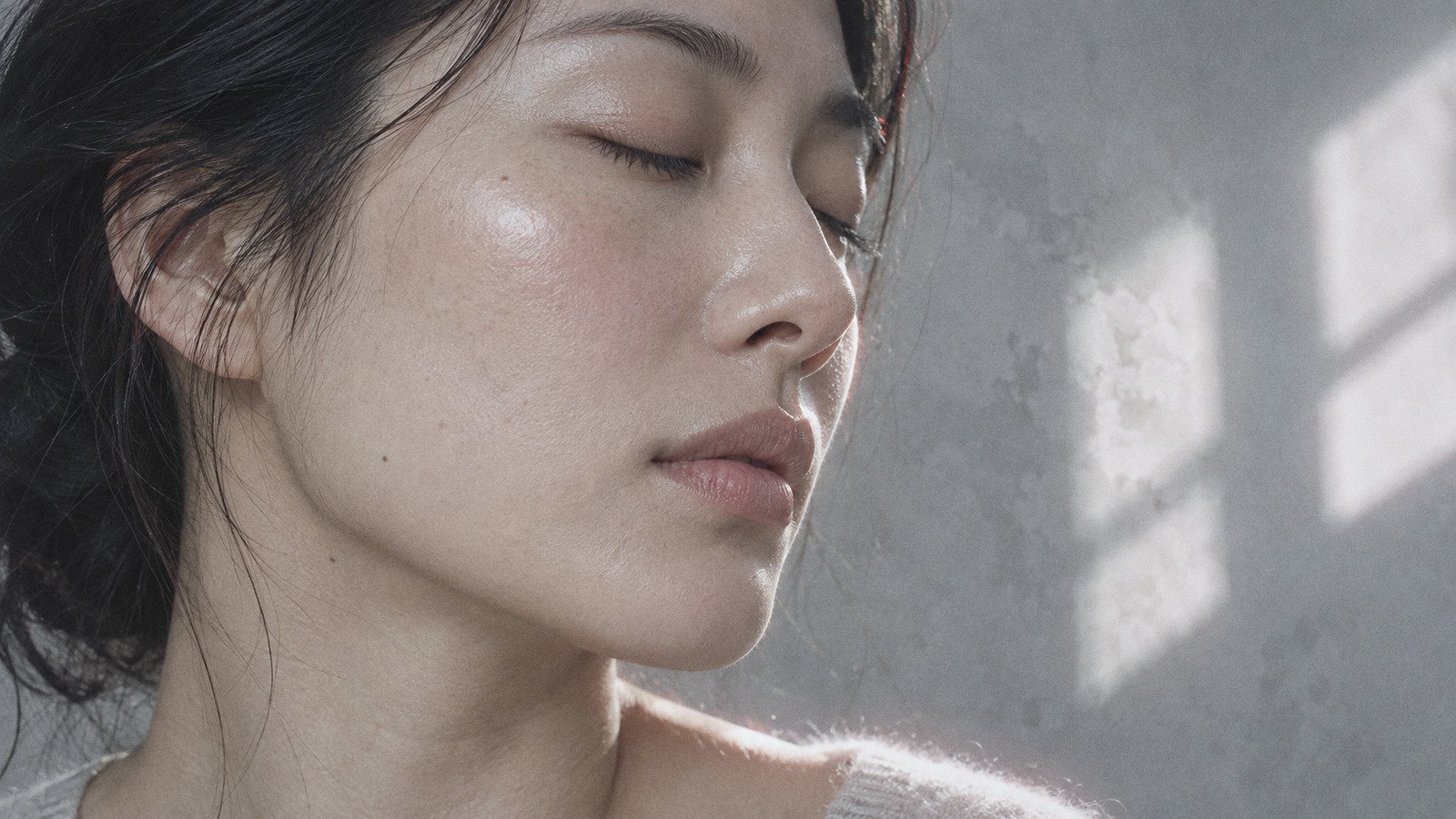 Close-up of a woman's cheek and jawline with natural skin texture in soft window light